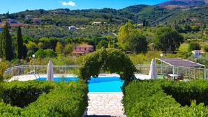 A swimming pool with a stone pathway, surrounded by greenery and a white fence.