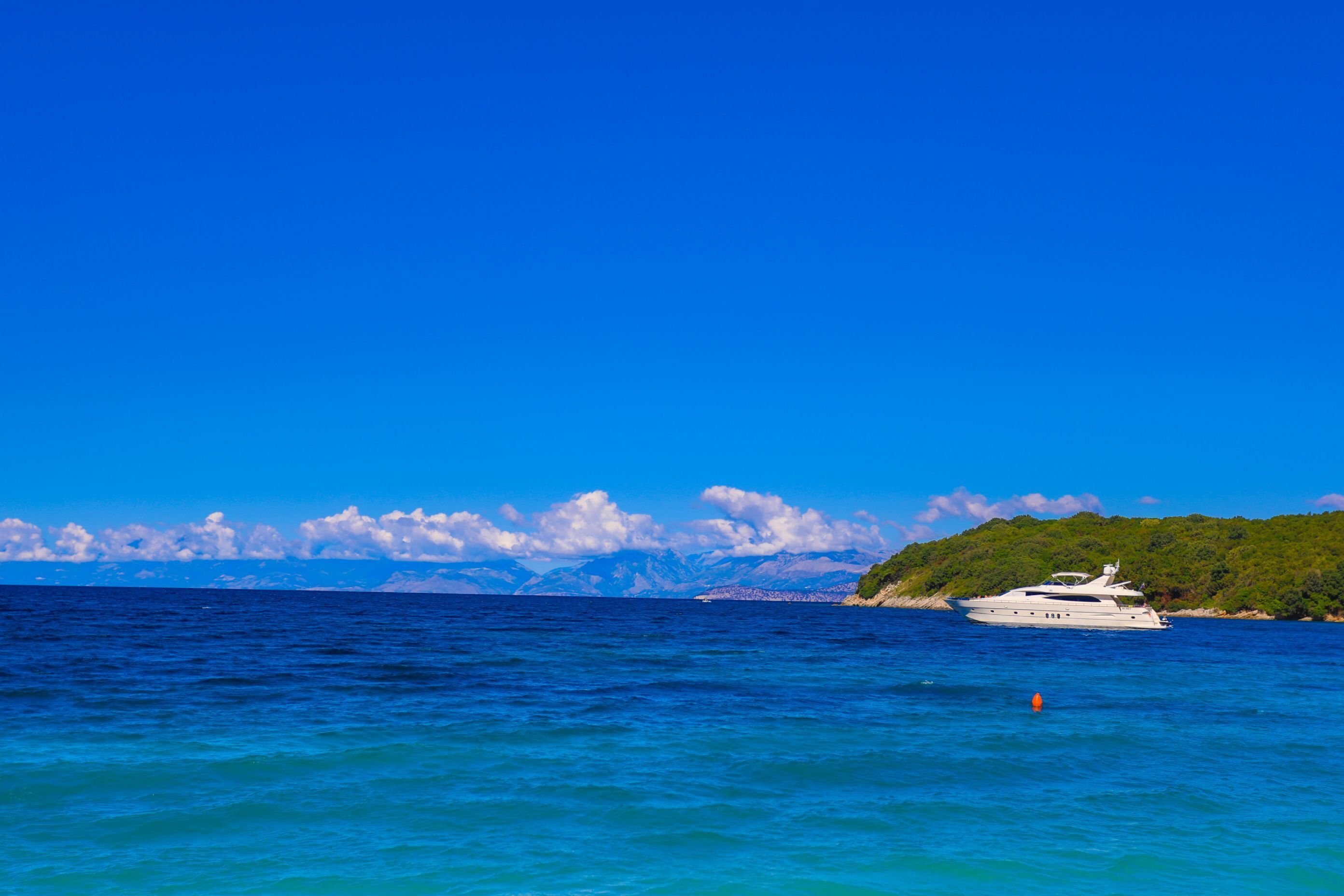 A yacht on a calm sea with a mountainous backdrop.