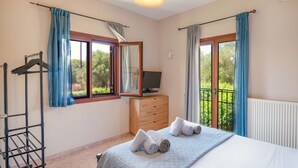Une chambre à coucher avec un lit, un téléviseur posé sur une commode en bois et un balcon avec des rideaux.