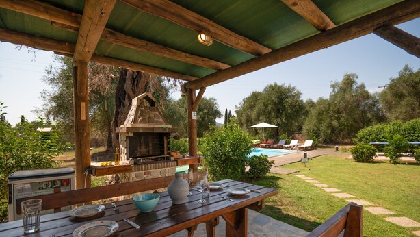 Un espace extérieur aménagé pour les repas, avec une table en pierre, des bancs en bois et un barbecue en pierre.