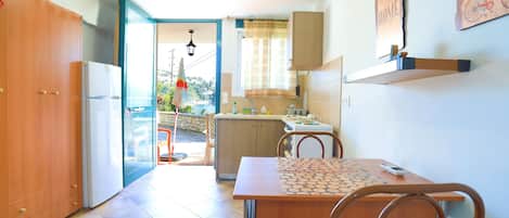A compact kitchen with a dining area, a refrigerator, a sink, and a window with curtains.