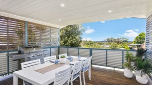 Une terrasse extérieure avec un barbecue, une table blanche, des chaises et des plantes en pot.