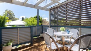 Un espace extérieur abrité, aménagé avec des chaises en osier et une table, entouré d’une terrasse en bois et de rampes en métal.