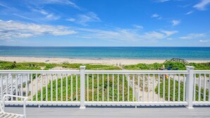 Une vue sur la plage depuis un balcon doté de balustrades blanches et d’une terrasse en bois.