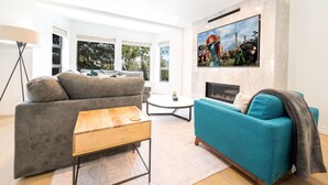 Ein modernes Wohnzimmer mit grauem Sofa, einem Sofa in Türkis, einem Holztisch und einem Kamin.