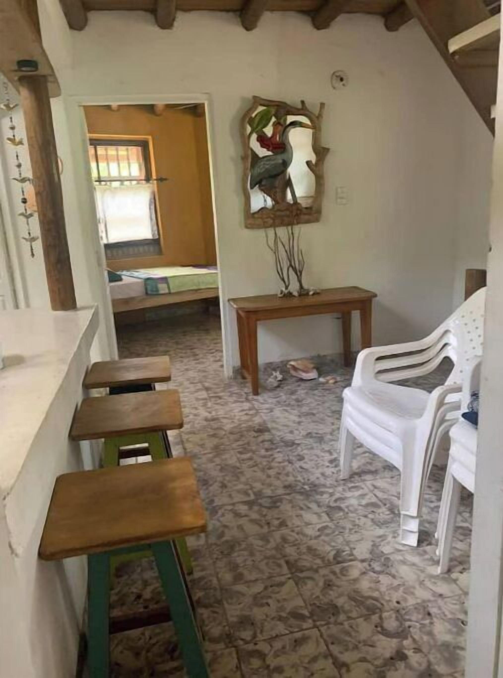 Una habitación con un banco de madera, una silla de plástico blanco y una pequeña mesa.