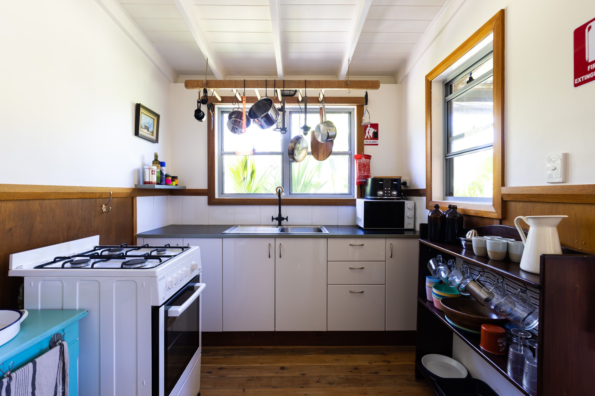 A kitchen with white cabinets, a stove, a microwave, and hanging pots.