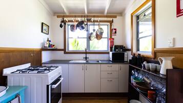 A kitchen with white cabinets, a stove, a microwave, and hanging pots.