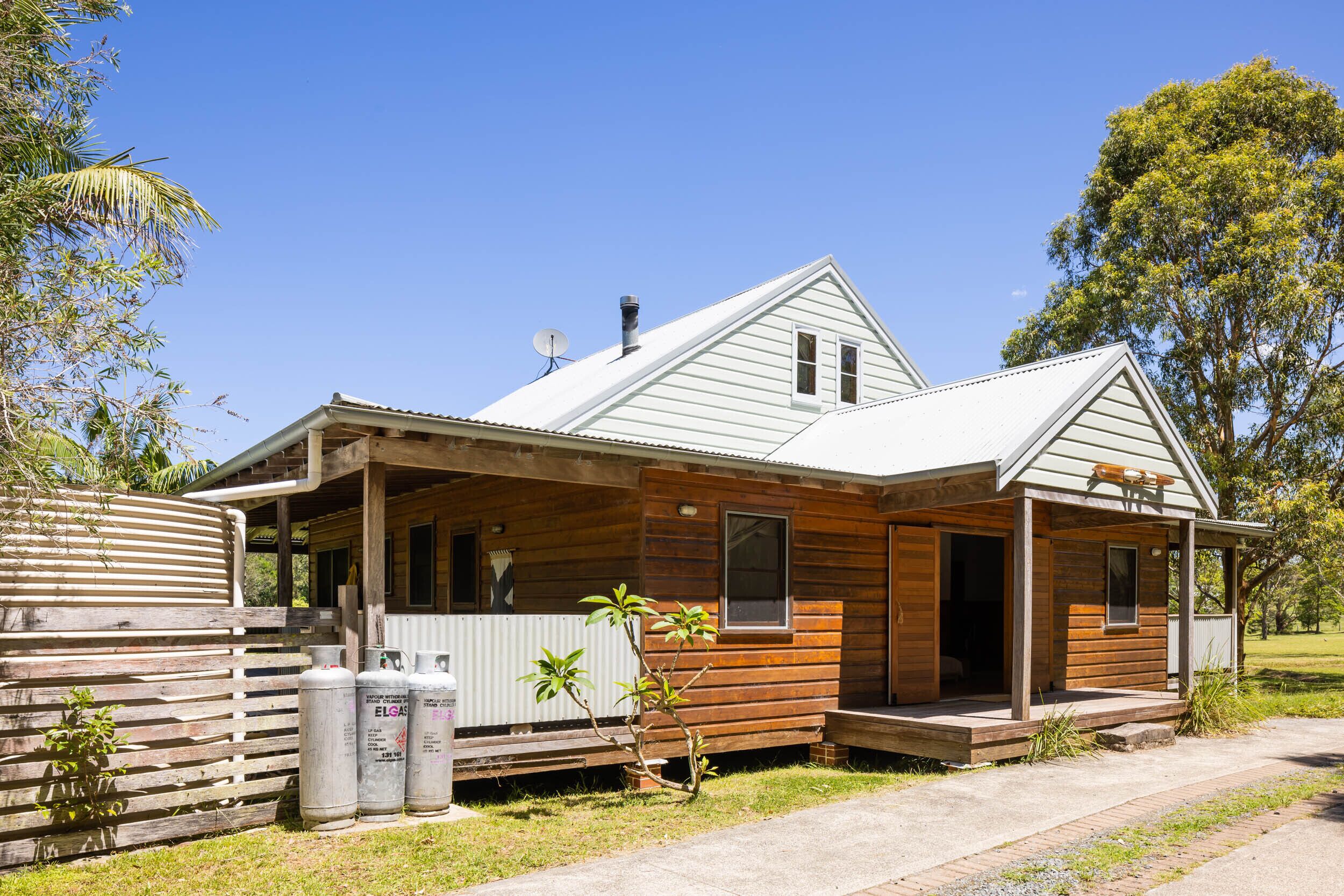 A wooden house with a porch, a satellite dish, and a small garden.