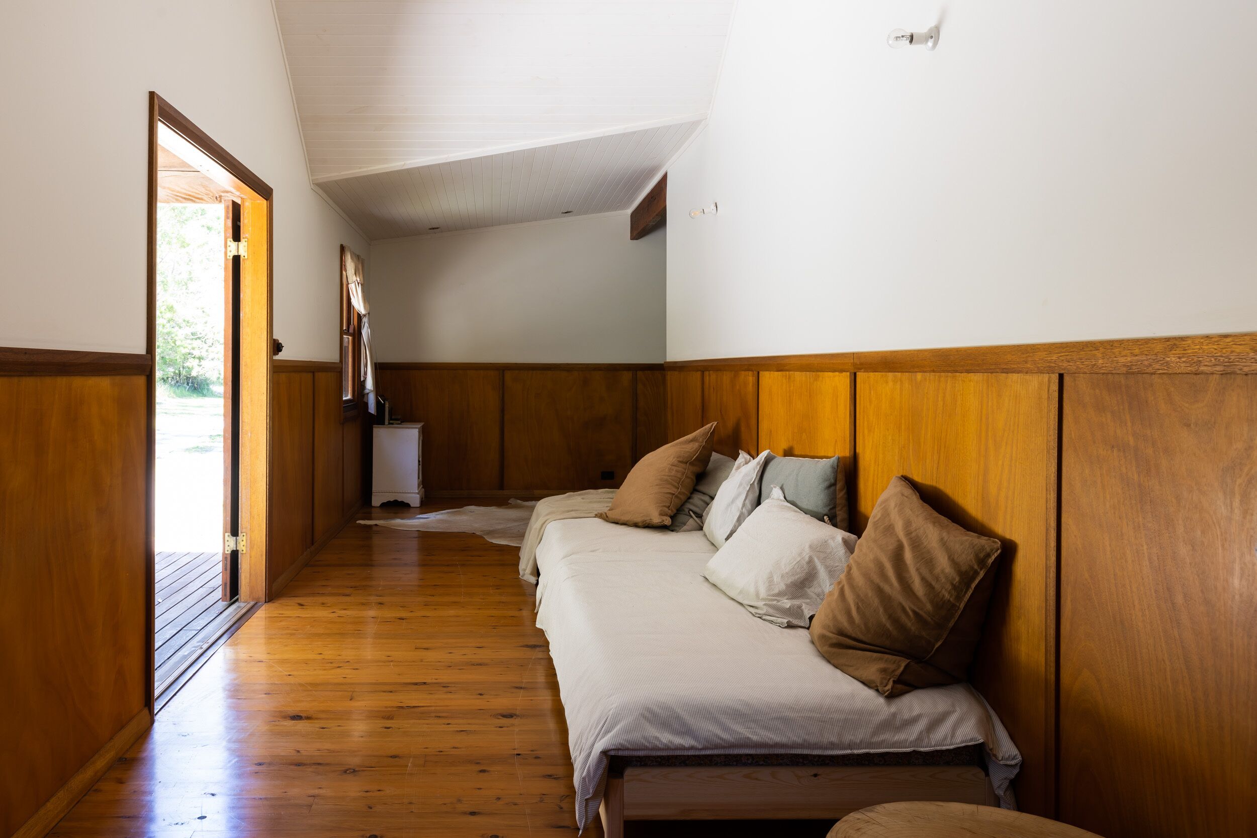 Une pièce avec un plancher en bois, un lit avec des oreillers, une tête de lit en bois et un plafond blanc.
