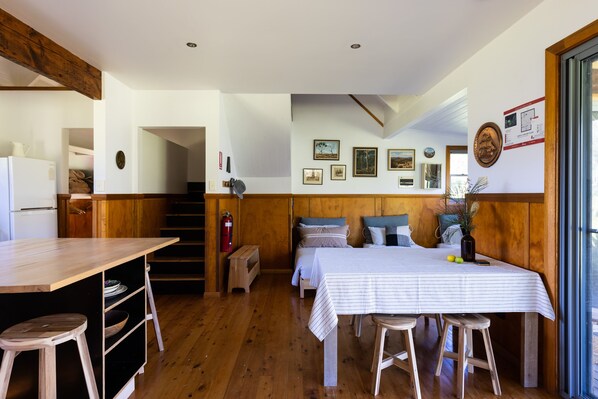 Une pièce chaleureuse avec un plancher en bois, un lit recouvert d’une courtepointe à rayures, une petite table avec des tabourets et un mur orné de tableaux encadrés.
