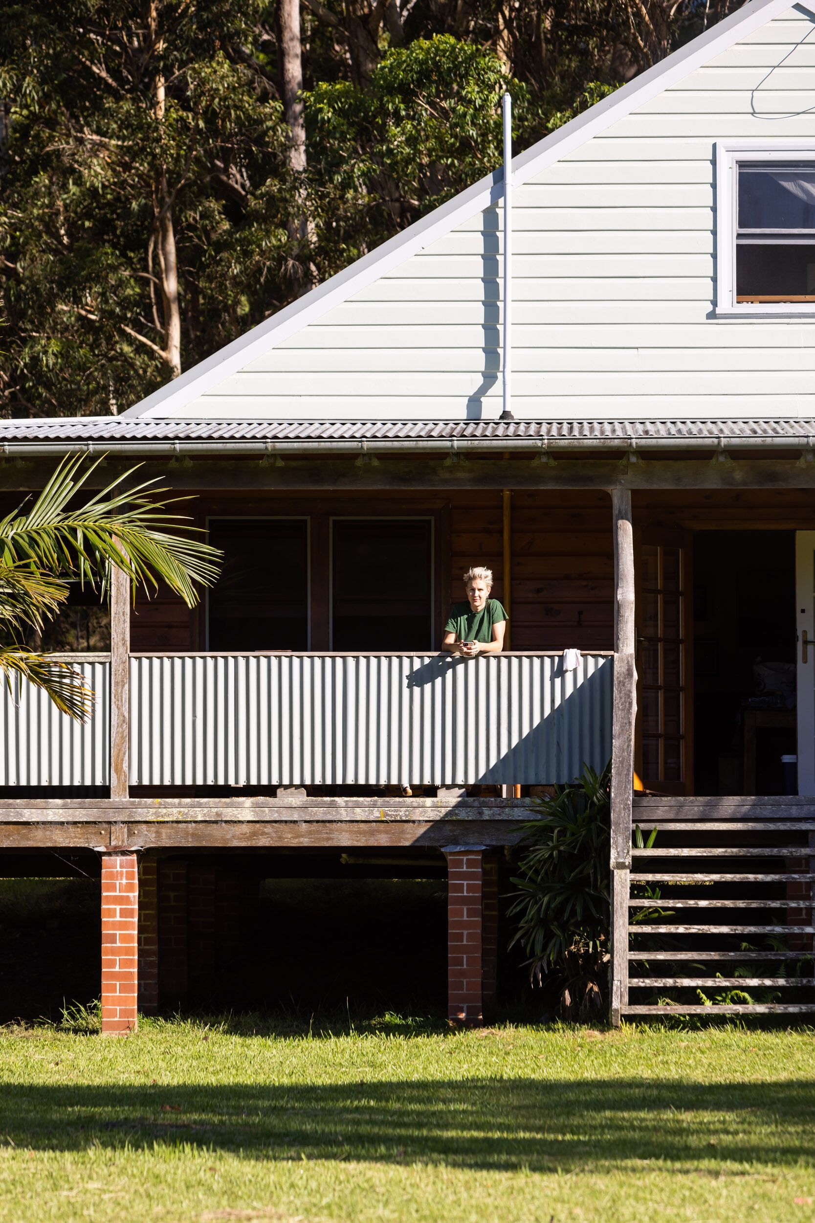 A two-story house with a balcony, a wooden porch, and a brick foundation.