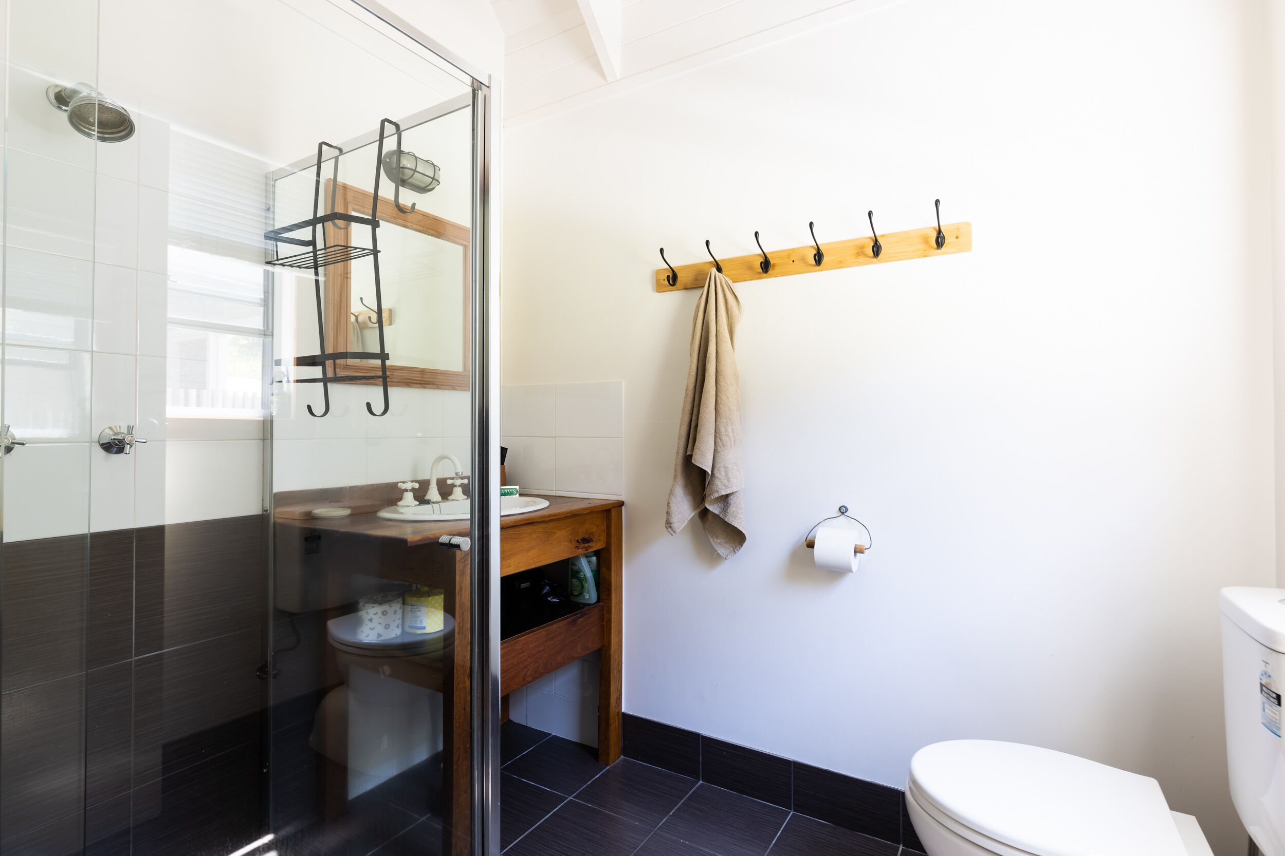 A bathroom with a glass shower enclosure, a wooden vanity, a towel rack, and a toilet.