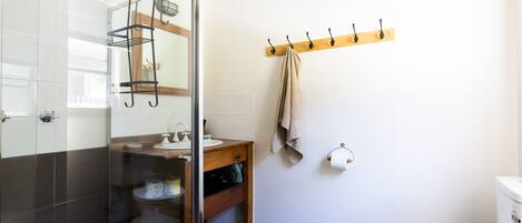 A bathroom with a glass shower enclosure, a wooden vanity, a towel rack, and a toilet.