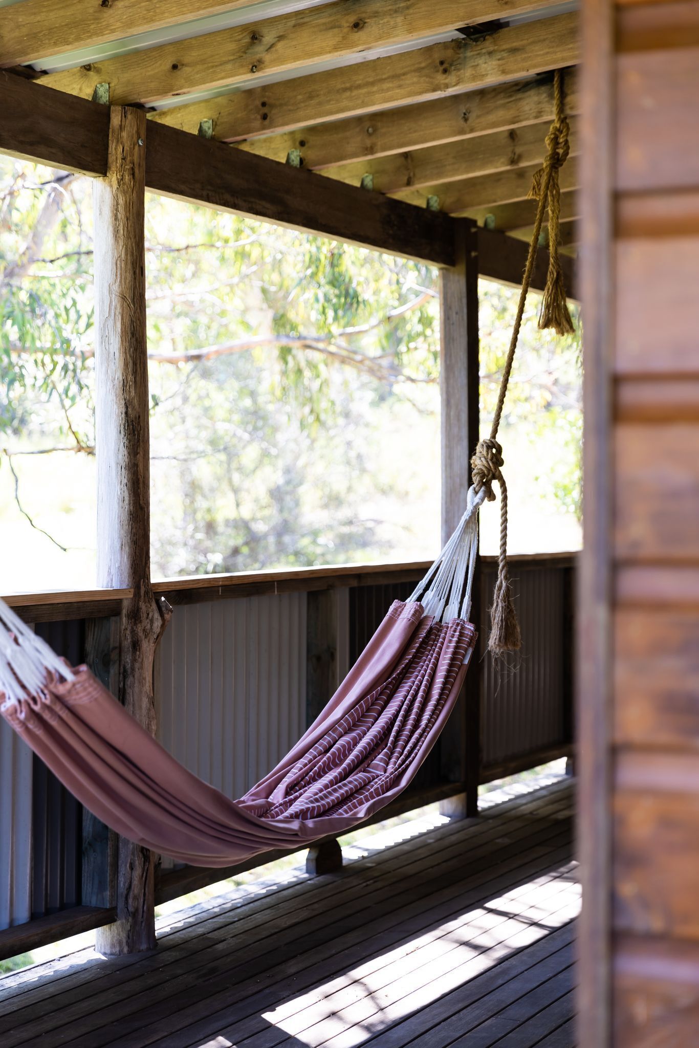 A wooden porch with a hammock hanging from a wooden beam.