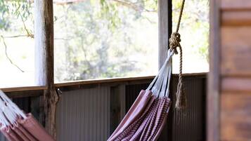 A wooden porch with a hammock hanging from a wooden beam.