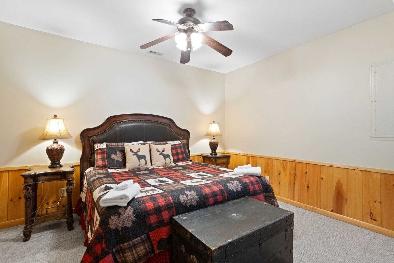 A bedroom with a wooden headboard, a quilt with animal prints, two bedside lamps, and a ceiling fan.