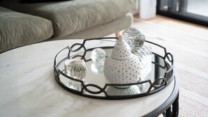 Una mesa redonda con superficie de vidrio y una bandeja de metal decorativa.