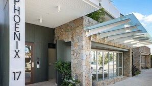 Una entrada moderna de edificio con fachada de piedra, puerta de cristal y un área exterior cubierta.