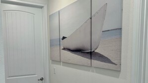 Un corridoio con una porta bianca, un pavimento in legno e un’opera d’arte appesa al muro raffigurante una barca su una spiaggia.