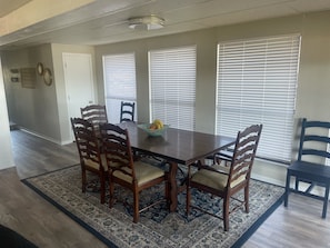 A dining area with a wooden table and chairs, a fruit bowl, and a patterned rug.