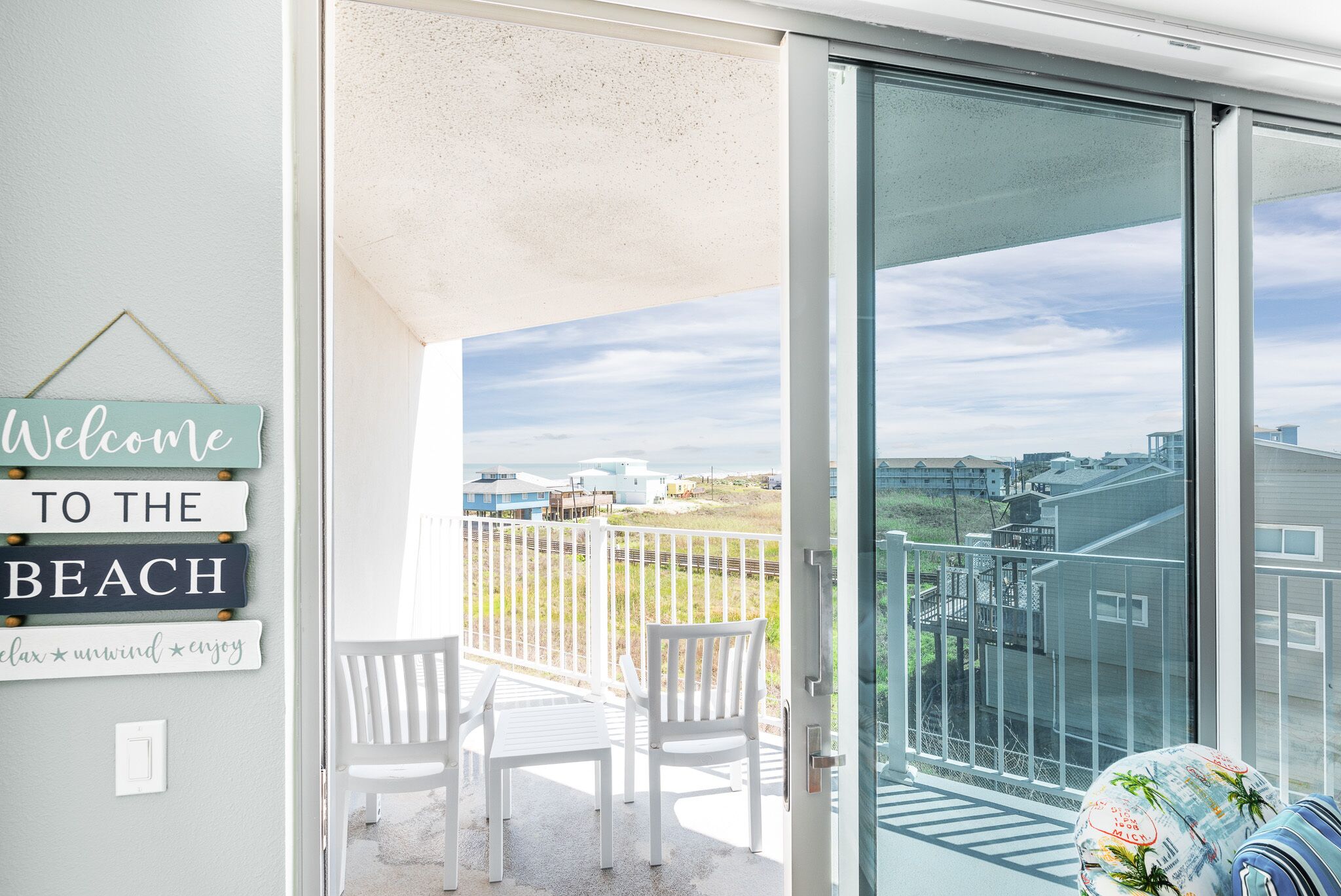 Een balkon met uitzicht op het strand, witte stoelen en een welkomstbord.