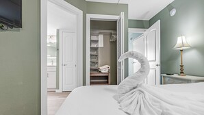 Une chambre d’hôtel comprenant un lit, une table de chevet, une lampe, une armoire et une porte ouverte donnant sur une salle de bain.