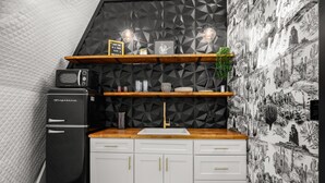 Cozinha compacta com geladeira preta, armários brancos, bancada de madeira e painel de backsplash com padrão geométrico.
