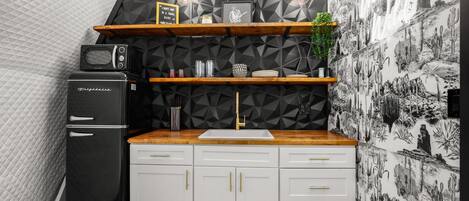 Una cocina compacta con un refrigerador negro, armarios blancos, encimera de madera y un salpicadero con estampado geométrico.