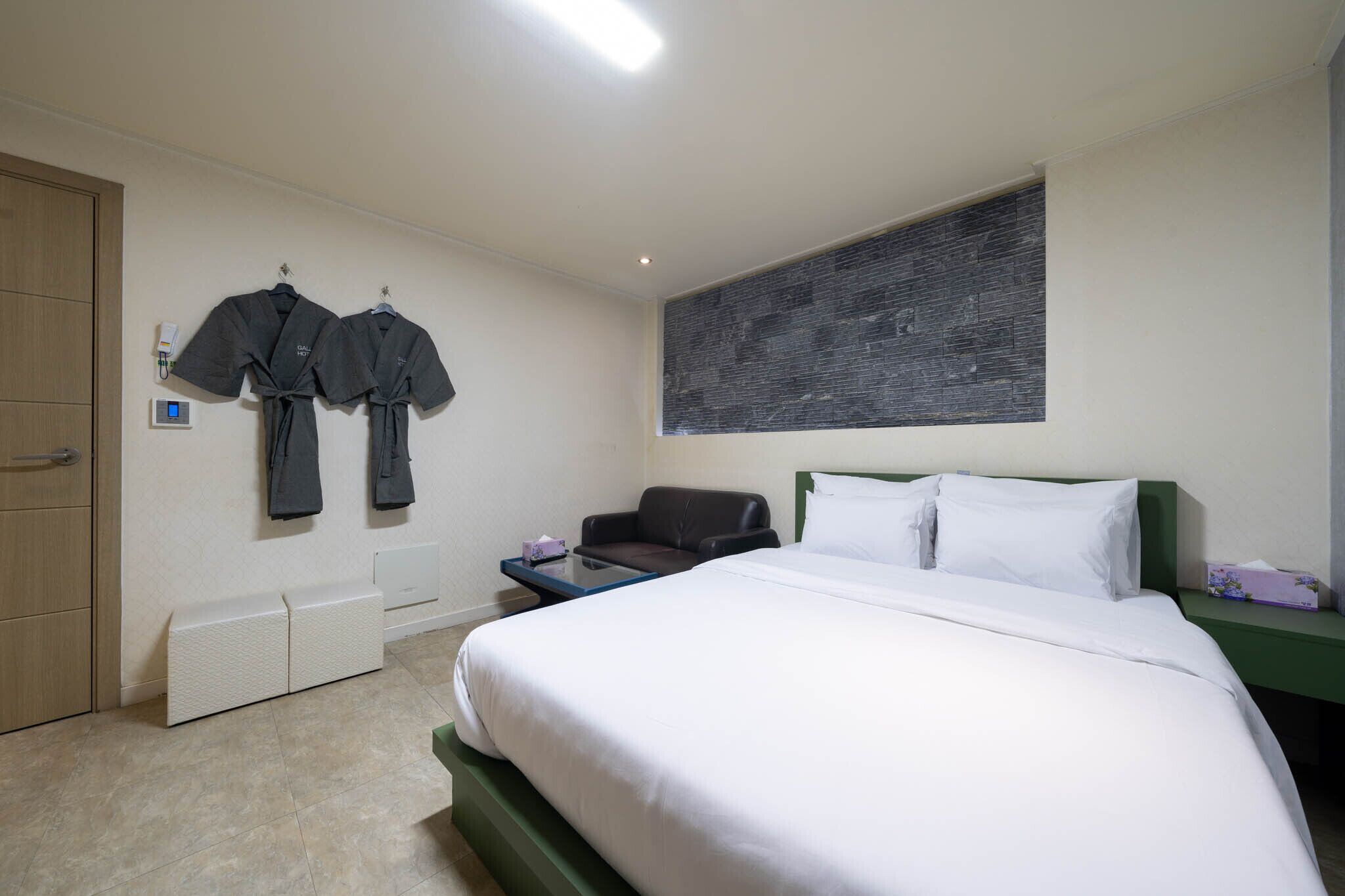 A hotel room with a bed, a desk, a chair, and two robes hanging on the wall.