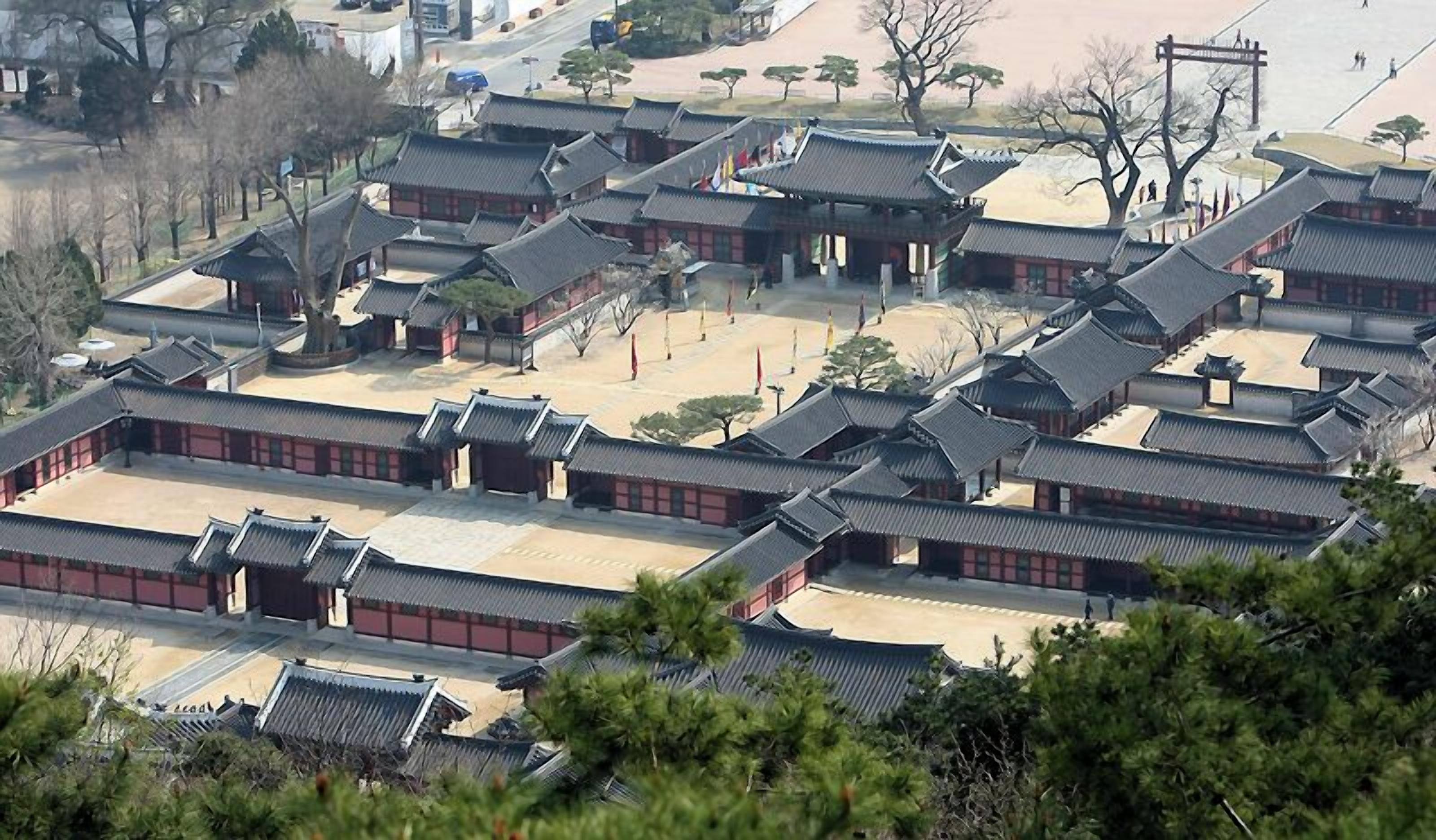 Ein traditioneller koreanischer Palastkomplex mit mehreren Gebäuden, die mit schindelartigen Dächern und roten Wänden versehen sind.