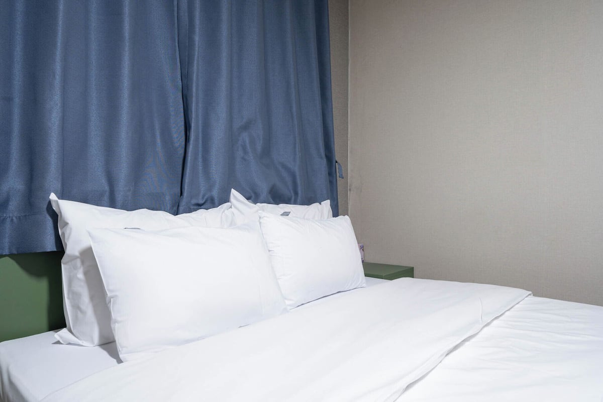 A neatly made bed with white bedding and pillows, a blue curtain, and a green nightstand.