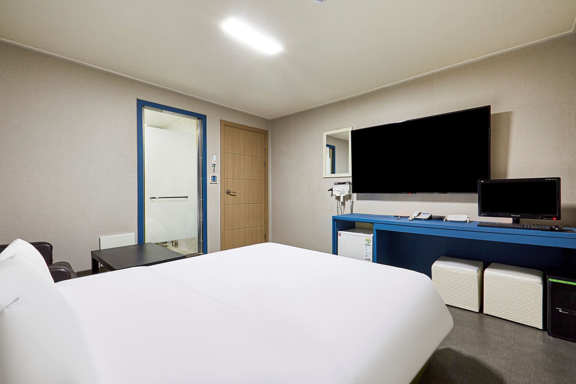 A hotel room with a bed, a desk with a computer, a TV, and a shower.