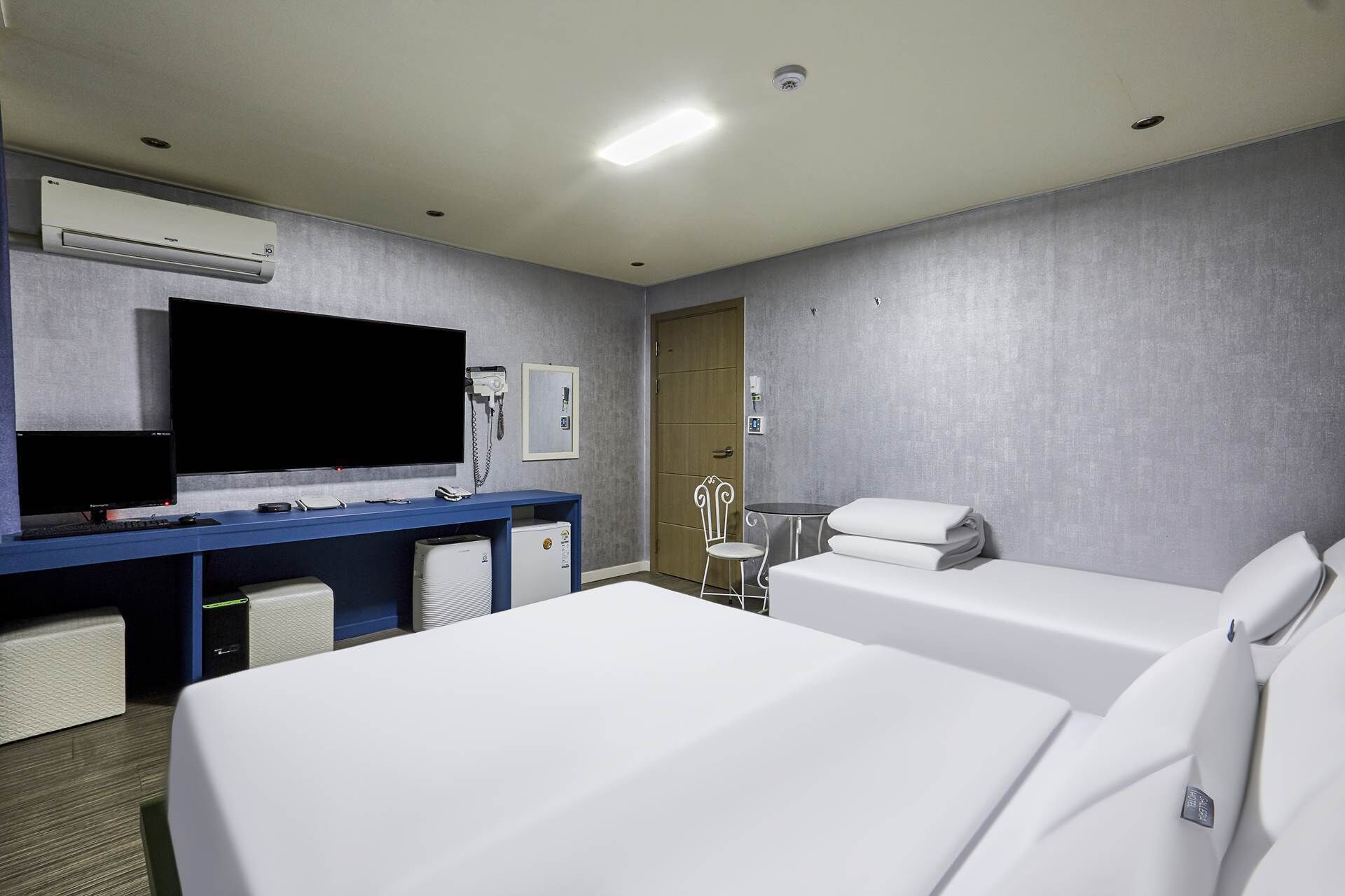 A hotel room with two beds, a desk with a flat-screen TV, a minibar, and a door leading to a bathroom.