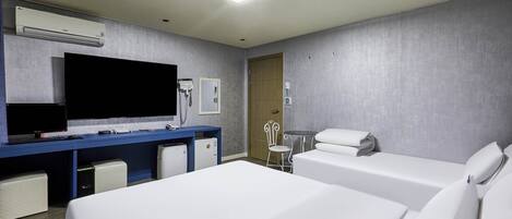 A hotel room with two beds, a desk with a flat-screen TV, a minibar, and a door leading to a bathroom.