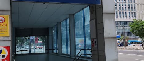 Une entrée d’immeuble avec une enseigne bleue indiquant la station de métro « Suwon City Hall » et une rampe d’accès pour les personnes à mobilité réduite.