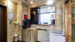 Un espace d’accueil avec un mur en marbre, un comptoir de réception, une machine à café, une poubelle et un réfrigérateur.