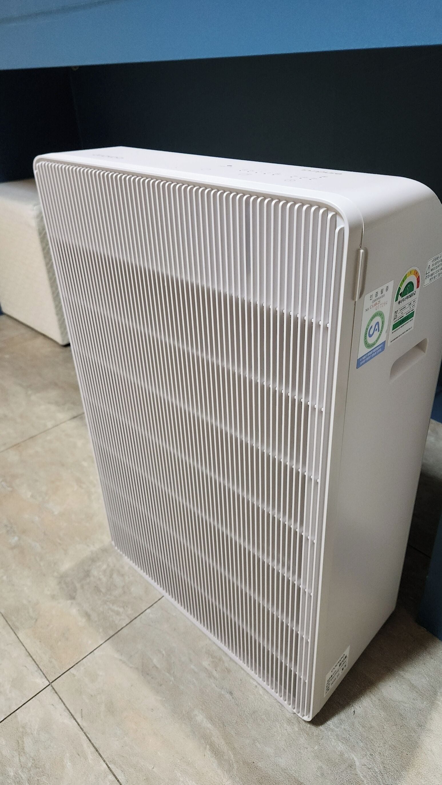 A white portable air conditioner with a vented front panel, stickers with safety and energy efficiency information, and a control panel on the right side.