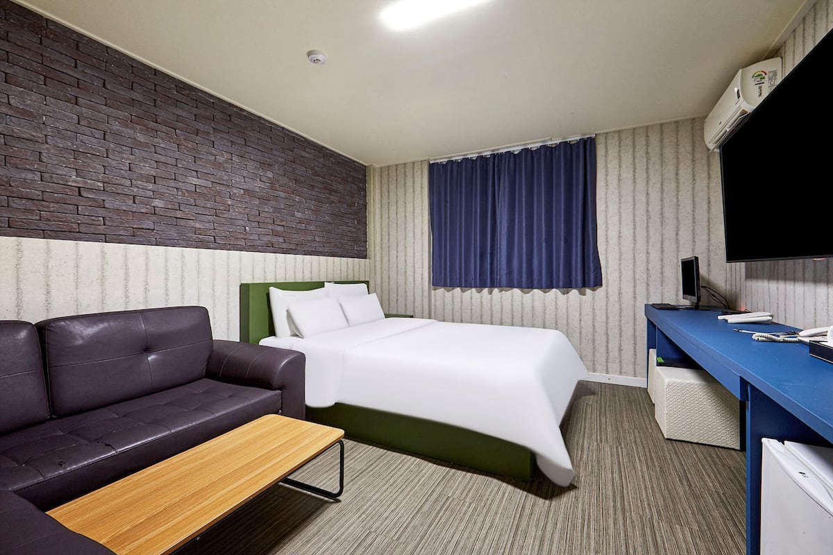 A hotel room with a bed, a sofa, a desk, and a television.