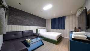Une chambre d’hôtel moderne équipée d’un canapé, d’un lit, d’une table basse en verre, d’un bureau avec une lampe et d’un téléviseur fixé au mur.
