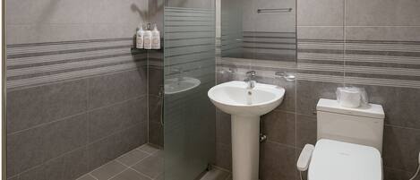 Un baño moderno con mampara de vidrio, lavabo pedestal y retrete.
