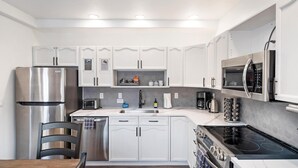 A modern kitchen with white cabinetry, stainless steel appliances, and a black countertop. - The Powderhound Condo (Whitefish)
