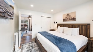 A bedroom with a large bed, a wooden headboard, a nightstand, a wall-mounted lamp, and a painting. - The Powderhound Condo (Whitefish)