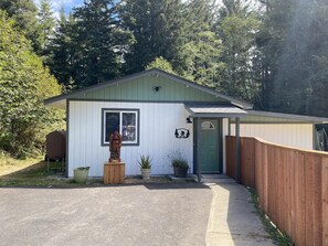 A small, single-story building with a green door, a window, and a 'Guest Parking' sign.