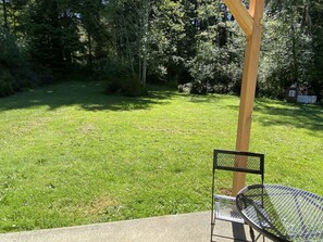 A grassy outdoor area with a metal table and chair, surrounded by trees and a wooden fence.