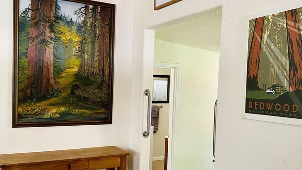Een gang met een houten bankje, een lijst met daarin een boslandschap en een schilderij van Redwood Nationaal Park.