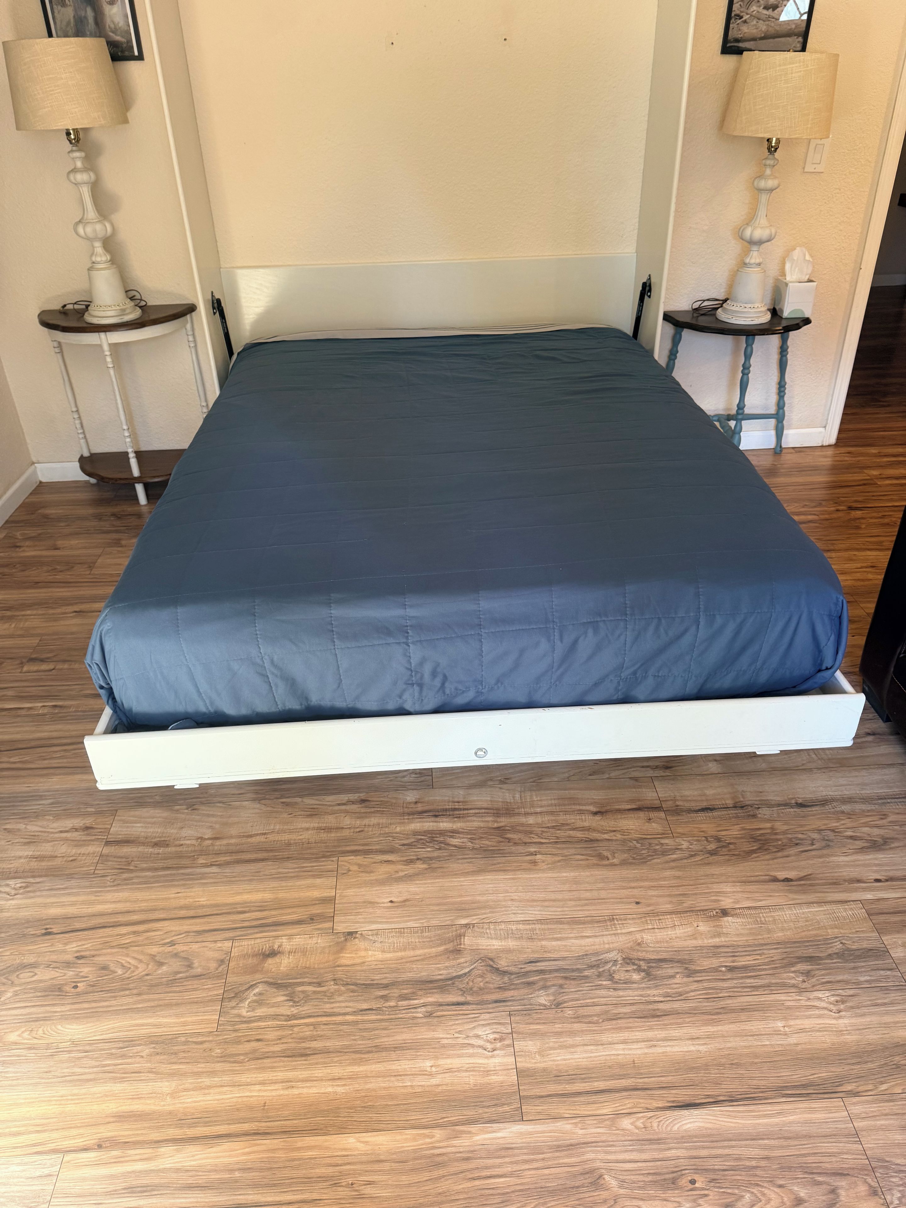 A bed with a white frame and a dark blue mattress in a room with wooden flooring and two bedside tables with lamps.