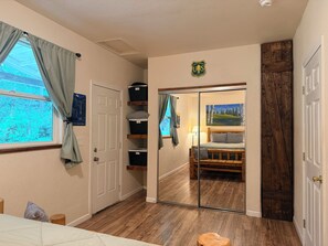 A room with a bed, a window with curtains, a door, a mirror, and a wall-mounted shelf with baskets. - Bigfoot Bungalow (Crescent City)
