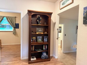 A corner room with a wooden bookshelf, a window with curtains, and a framed artwork on the wall.