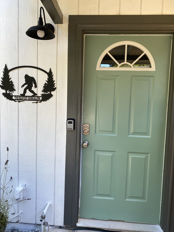 A green door with a white-framed window, a wall-mounted light fixture, and a doorbell.